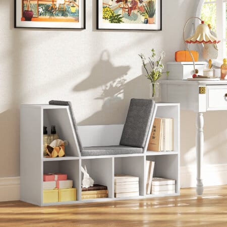 Ein weisses Bücherregal mit 6 Fächern und einem Sitzkissen in Leinenoptik.