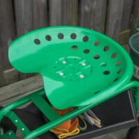 Ein grüner Gartenwagen mit Drehsitz und Ablagekorb.