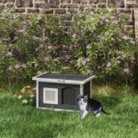 Graues wetterfestes Katzenhaus aus Holz mit integrierter Kratzmatte und Klappdach, bietet Schutz und Krallenpflege im Freien.