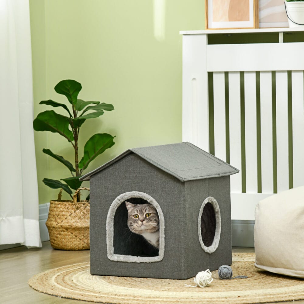 Graue Katzenhöhle in Hausform mit bequemem Kissen und zwei Türen, bietet einen gemütlichen Rückzugsort für Katzen.