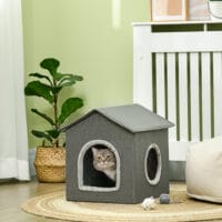 Graue Katzenhöhle in Hausform mit bequemem Kissen und zwei Türen, bietet einen gemütlichen Rückzugsort für Katzen.