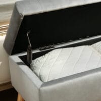Graue Sitzbank mit stilvoller Samtoptik, integriertem Stauraum und Beinen aus massivem Gummiholz, perfekt für moderne Wohnräume.