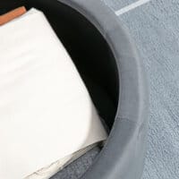 Ein grauer Sitzhocker mit Stauraum in runder Form und Samtoptik.